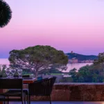 Table dressée sur la terrasse de l'Hôtel Villa Padulaccia au crépuscule, ciel rose au-dessus de la mer et de la tour de l'île de Pinarellu
