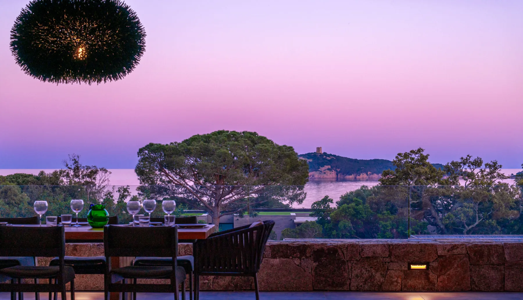 Table dressée sur la terrasse de l'Hôtel Villa Padulaccia au crépuscule, ciel rose au-dessus de la mer et de la tour de l'île de Pinarellu