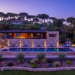 L'Hôtel Villa Padulaccia et sa piscine éclairés au crépuscule, pins parasols sur un ciel mauve