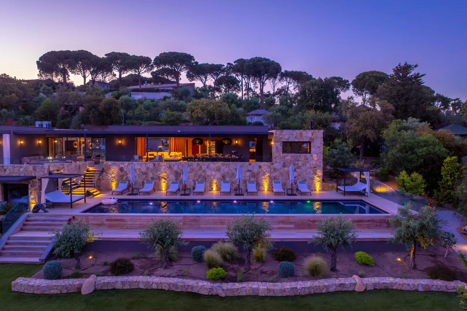 L'Hôtel Villa Padulaccia et sa piscine éclairés au crépuscule, pins parasols sur un ciel mauve