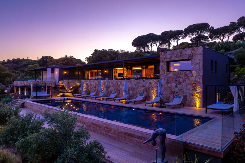 Piscine chauffée et terrasses éclairées de l'Hôtel Villa Padulaccia au crépuscule, statue de plongeur au bord de l'eau