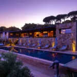 Piscine chauffée et terrasses éclairées de l'Hôtel Villa Padulaccia au crépuscule, statue de plongeur au bord de l'eau
