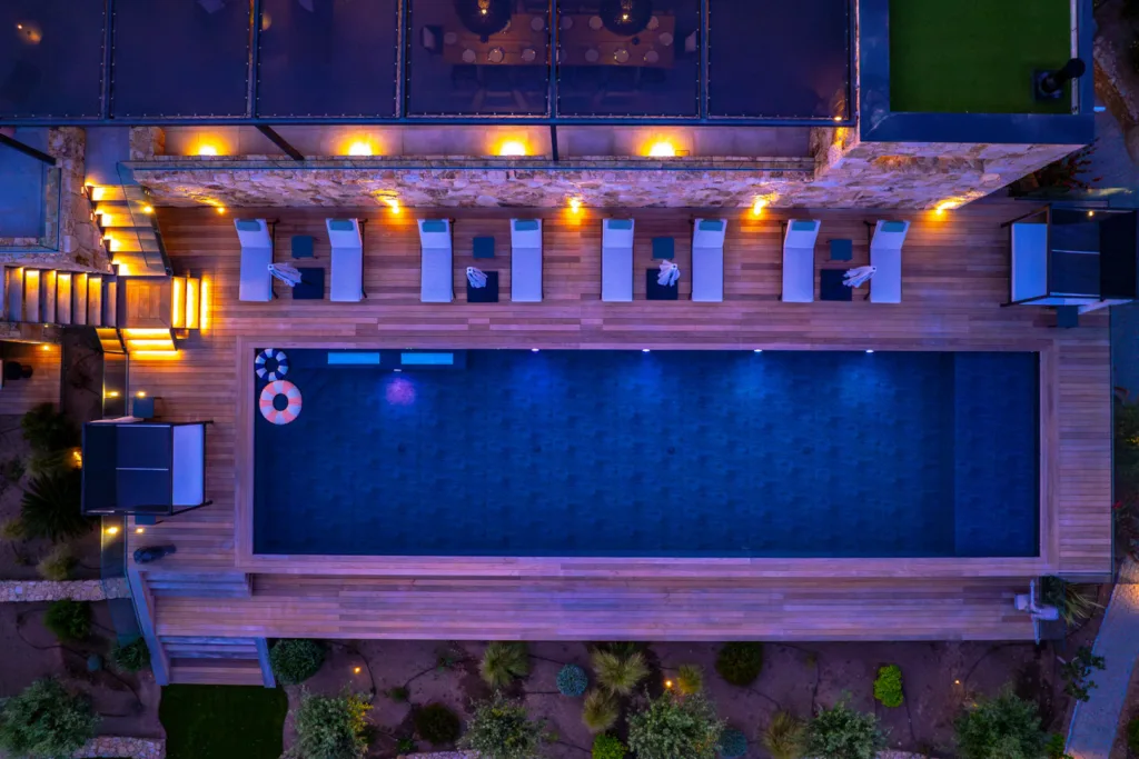 Piscine chauffée de l'Hôtel Villa Padulaccia vue du ciel à la nuit tombée, transats et lampes allumées