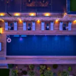 Piscine chauffée de l'Hôtel Villa Padulaccia vue du ciel à la nuit tombée, transats et lampes allumées
