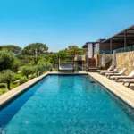 Piscine chauffée de l'Hôtel Villa Padulaccia au niveau de l'eau, transats et parasols fermés le long du mur de pierre