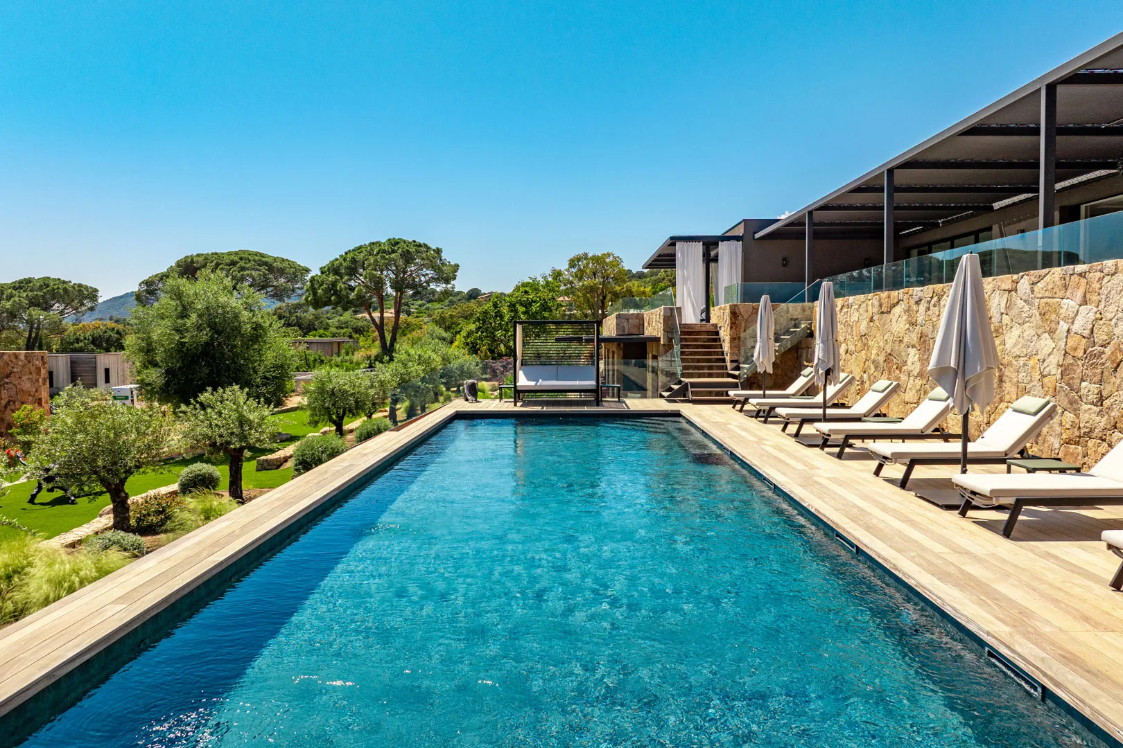 Piscine chauffée de l'Hôtel Villa Padulaccia au niveau de l'eau, transats et parasols fermés le long du mur de pierre
