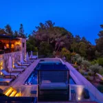 Piscine de l'Hôtel Villa Padulaccia au crépuscule, transats le long de la terrasse éclairée et pins alentour