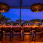 Longue table dressée sous la pergola de l'Hôtel Villa Padulaccia à l'heure bleue, verres alignés et suspensions allumées
