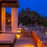 Chambre éclairée et lit de repos sur la terrasse de l'Hôtel Villa Padulaccia à la nuit tombée, rideaux blancs