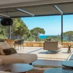 Salon de la terrasse couverte de l'Hôtel Villa Padulaccia, canapés et fauteuils tournés vers la mer et la tour de l'île de Pinarellu