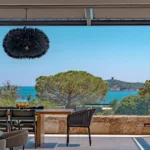 Grande table de la terrasse couverte de l'Hôtel Villa Padulaccia face à la mer, suspension noire et tour génoise au loin