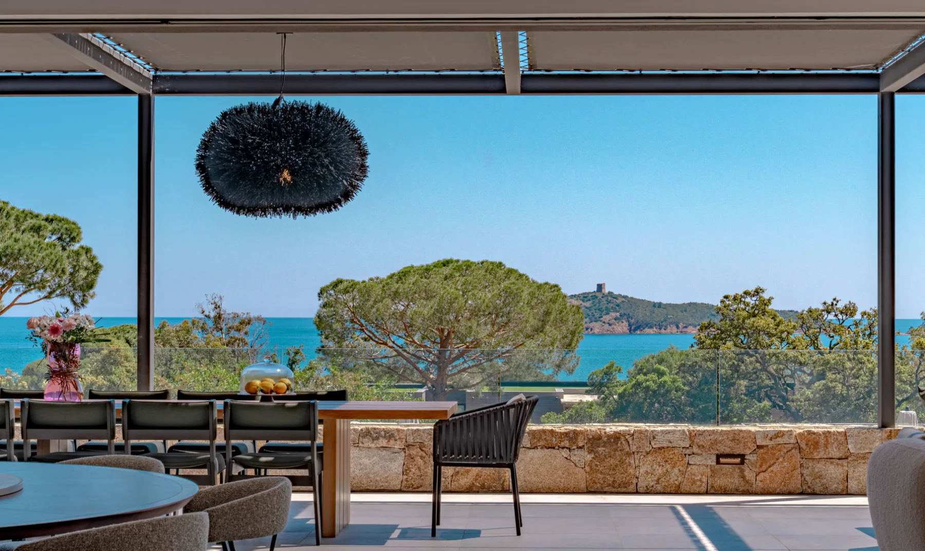 Grande table de la terrasse couverte de l'Hôtel Villa Padulaccia face à la mer, suspension noire et tour génoise au loin