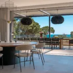 Salle à manger de l'Hôtel Villa Padulaccia ouverte sur la terrasse et la mer, table ronde et suspensions