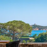Vue depuis une terrasse de l'Hôtel Villa Padulaccia : pin parasol, mer turquoise et tour génoise de l'île de Pinarellu