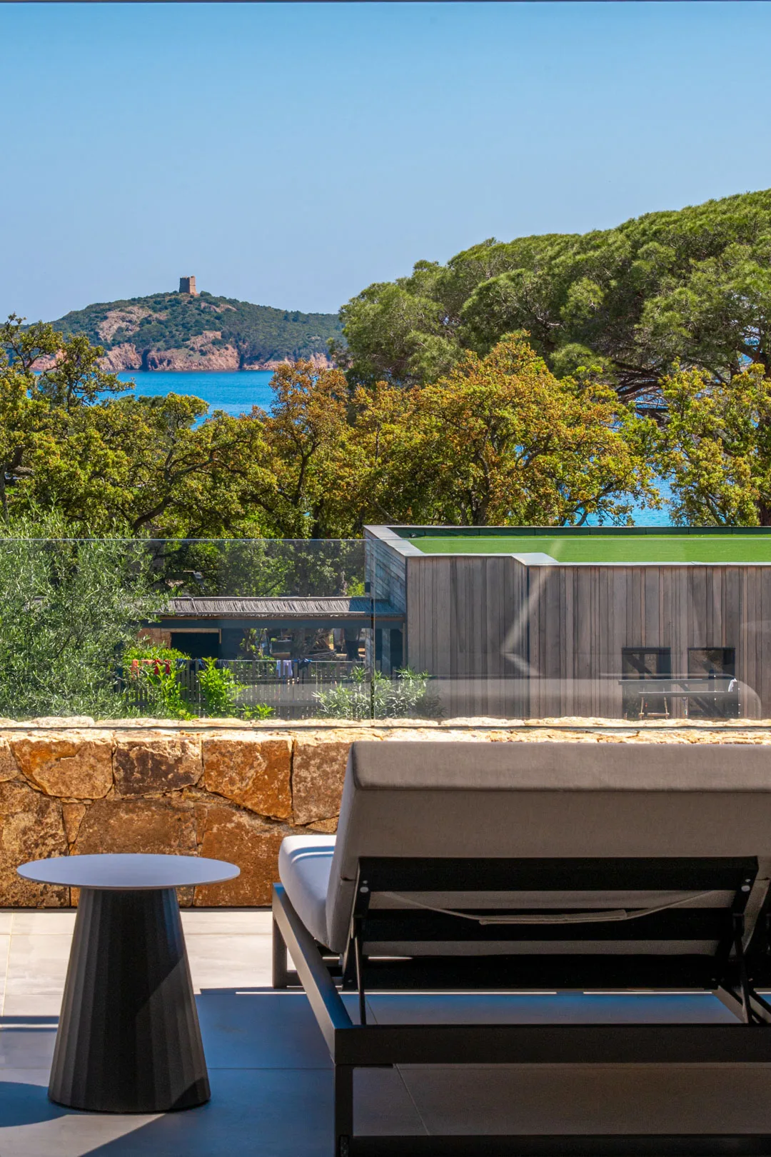 Lit de repos et table d'appoint sur une terrasse de l'Hôtel Villa Padulaccia, tour génoise et mer au-delà des pins
