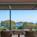 Deux fauteuils tournés vers la mer sous la pergola de l'Hôtel Villa Padulaccia, tour de l'île de Pinarellu au loin
