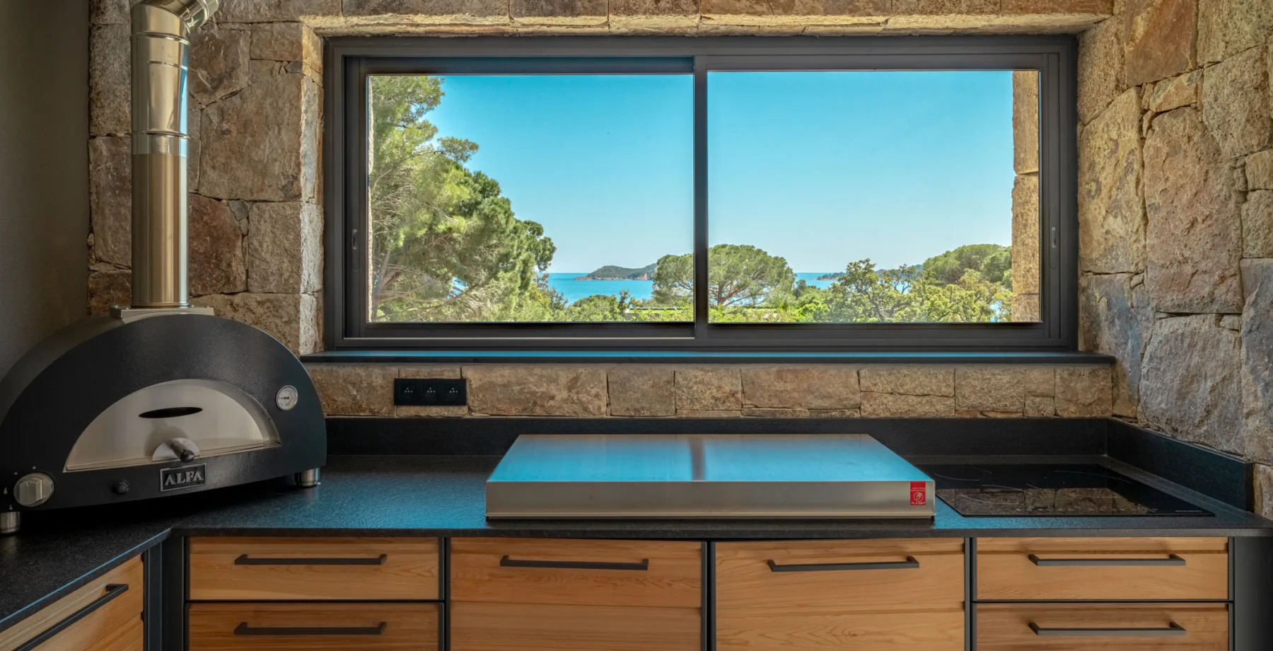 Plan de travail et four à pizza sous une fenêtre ouverte sur les pins et la mer, Hôtel Villa Padulaccia
