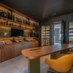Bureau-bibliothèque de l'Hôtel Villa Padulaccia : table en bois, fauteuils en cuir, étagères de livres et de bouteilles, caves à vin éclairées