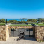 Toits végétalisés et façade de pierre de l'Hôtel Villa Padulaccia, la mer et la tour de l'île de Pinarellu en arrière-plan