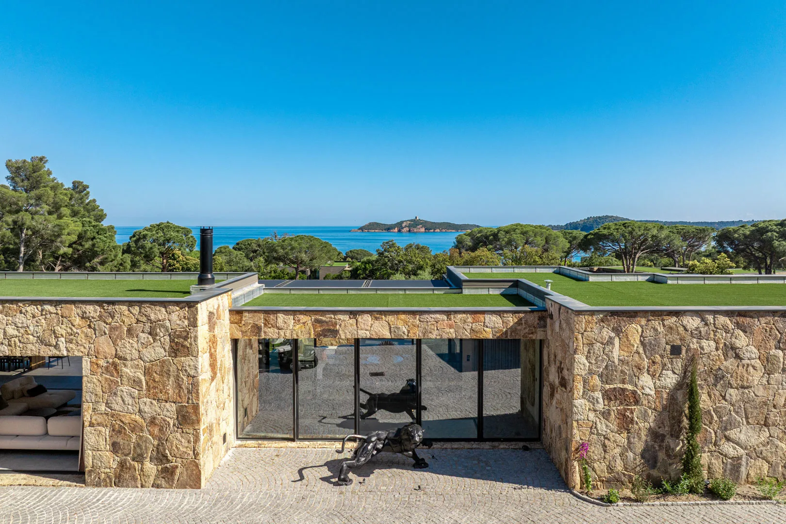 Toits végétalisés et façade de pierre de l'Hôtel Villa Padulaccia, la mer et la tour de l'île de Pinarellu en arrière-plan