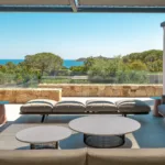 Salon extérieur couvert de l'Hôtel Villa Padulaccia, canapés gris et tables basses face aux pins et à la mer
