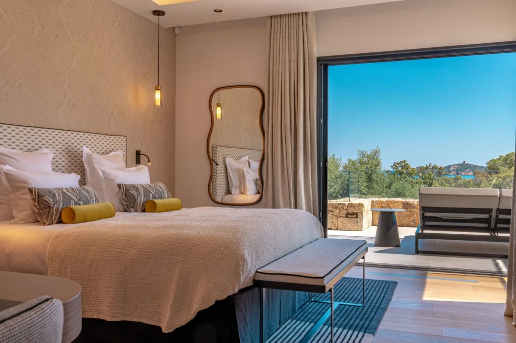 Suite Pays des Merveilles de l'Hôtel Villa Padulaccia, lit, miroir aux formes arrondies et baie vitrée ouverte sur la terrasse et la mer