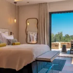 Suite Pays des Merveilles de l'Hôtel Villa Padulaccia, lit, miroir aux formes arrondies et baie vitrée ouverte sur la terrasse et la mer