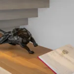 Sculpture de panthère noire et beau livre ouvert sur un dessin de bijou, posés sur une étagère en bois sous l'escalier de l'Hôtel Villa Padulaccia