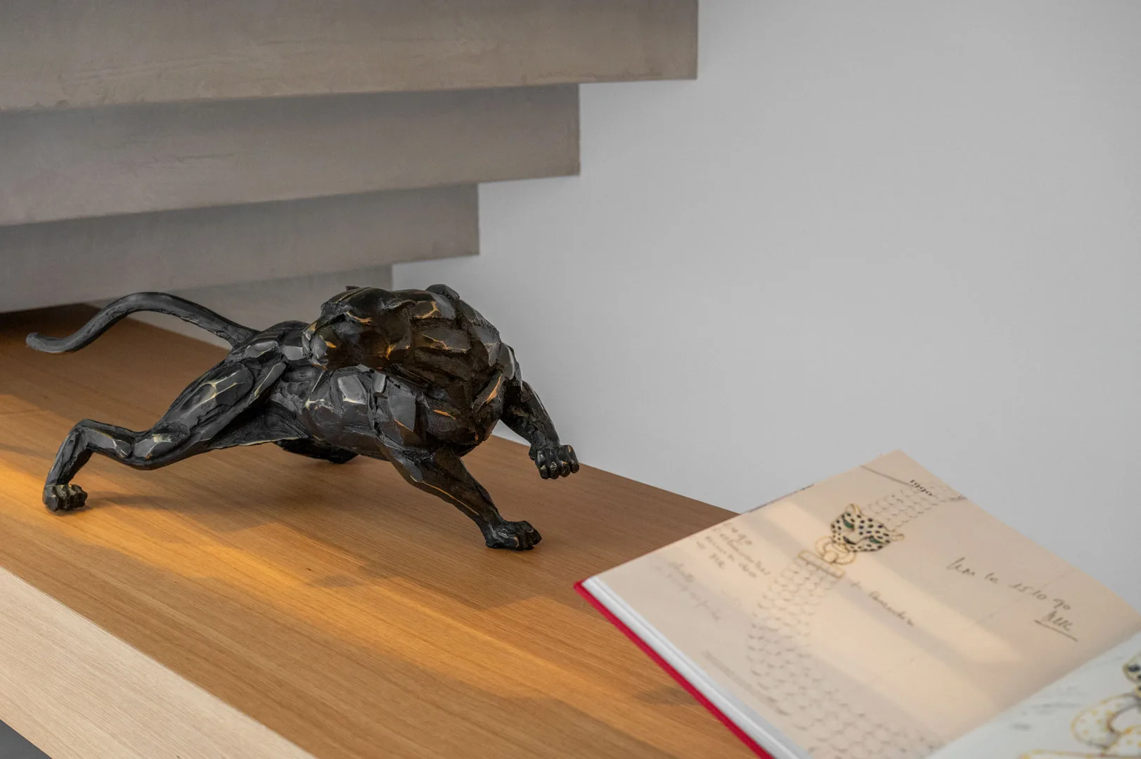 Sculpture de panthère noire et beau livre ouvert sur un dessin de bijou, posés sur une étagère en bois sous l'escalier de l'Hôtel Villa Padulaccia