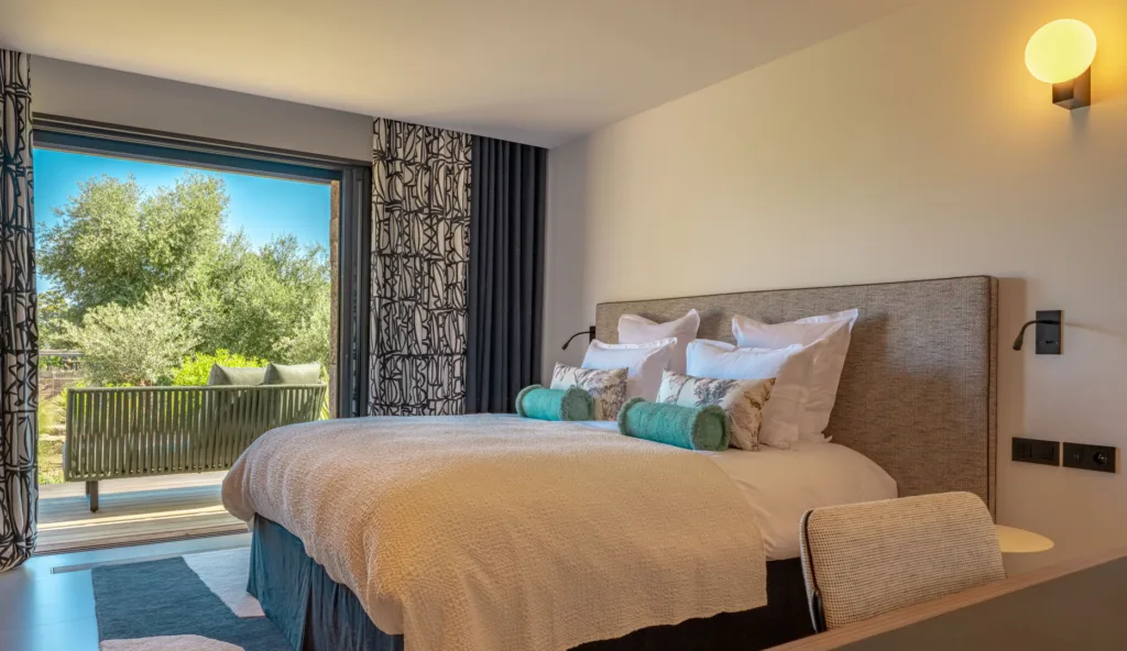 Suite Carnet de Voyage de l'Hôtel Villa Padulaccia, lit et baie vitrée ouverte sur la terrasse et les oliviers