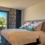 Suite Carnet de Voyage de l'Hôtel Villa Padulaccia, lit et baie vitrée ouverte sur la terrasse et les oliviers