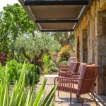 Terrasse en bois au pied d'un mur de pierre, fauteuils roses face au jardin de l'Hôtel Villa Padulaccia