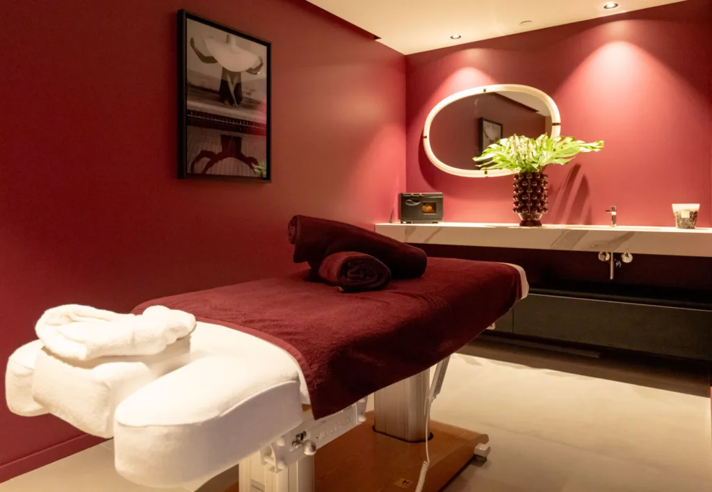Salle de massage du spa de l'Hôtel Villa Padulaccia, table de soin drapée de bordeaux, serviettes blanches et murs rouge profond